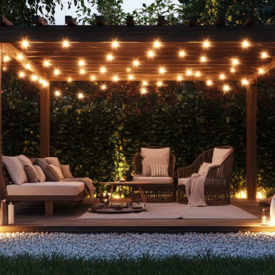 Simple garden pergola with patio furniture on gravel under string lights Epic Landscape Lighting